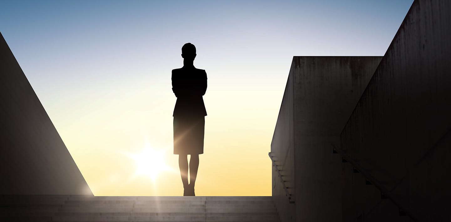 Silhouette of a woman at the top of steps looking at the setting or rising sun