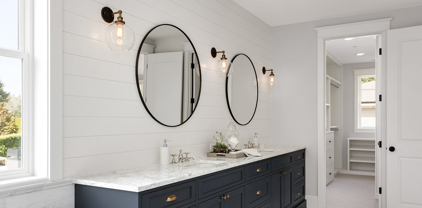Bathroom with shiplap walls, circular mirrors, and a navy blue vanity.