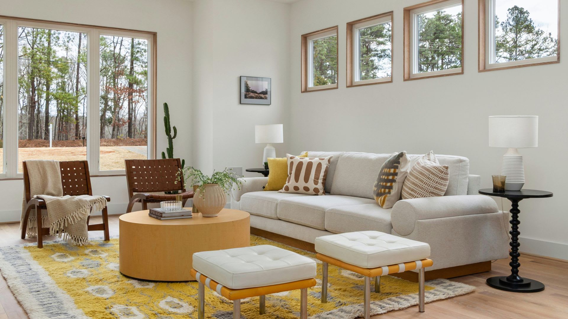 Sunlit living room styled in 2026 summer design trends with butter yellow accents, natural wood, and woven leather chairs.
