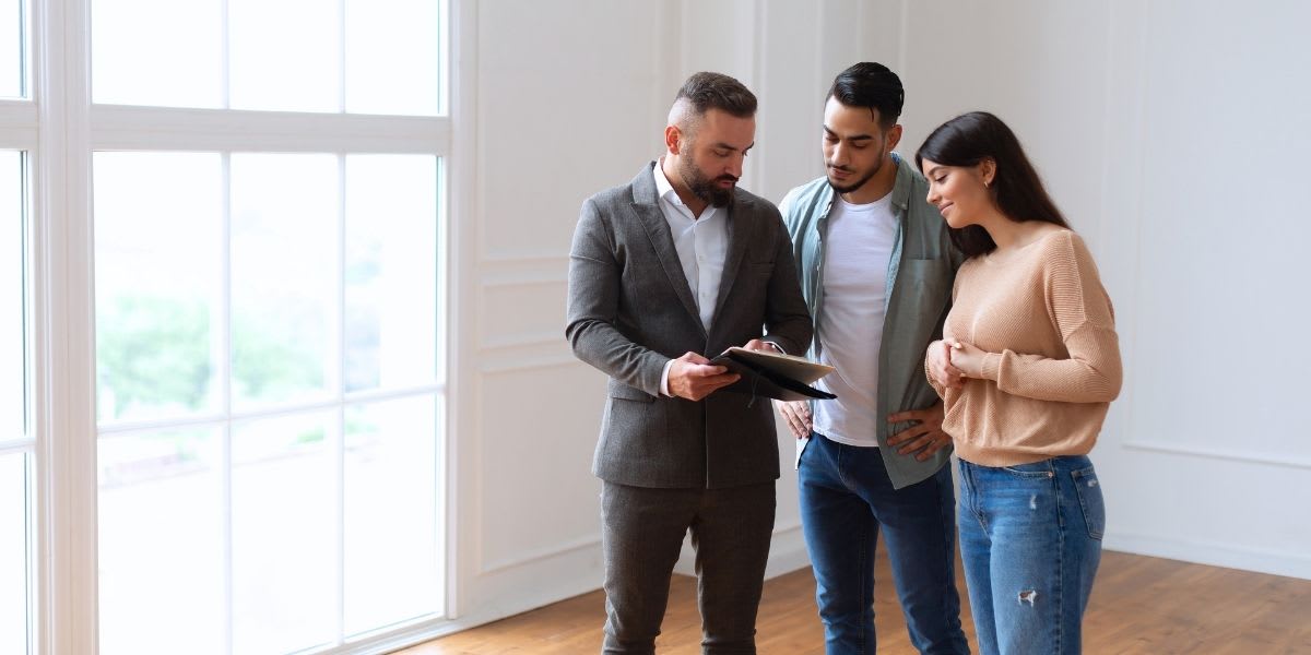 Agent conducting a pre-listing walk-through Real estate agent reviewing notes on a clipboard with two clients in an empty room