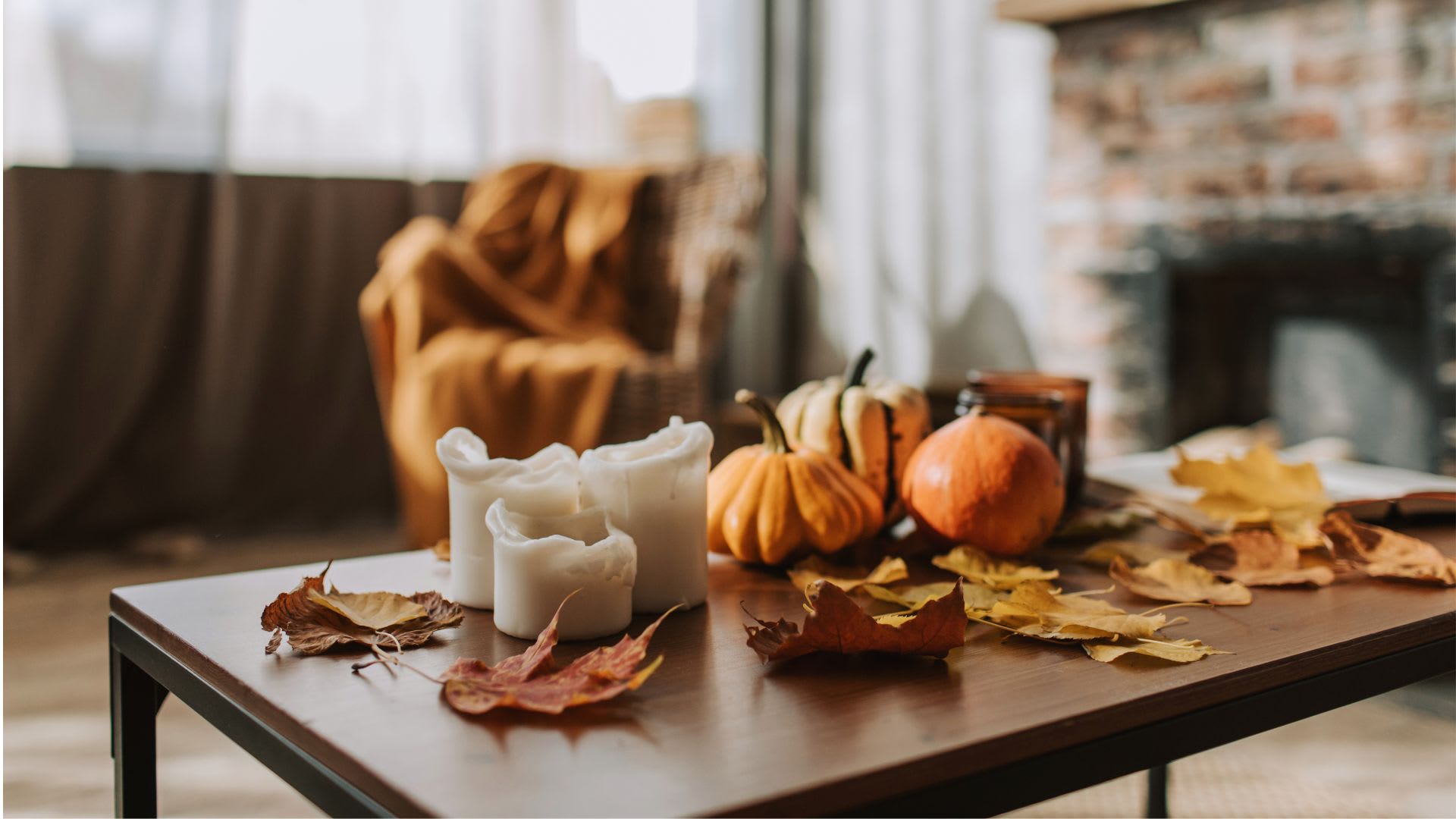 Coffee table with small pumpkins, white pillar candles and autumn leaves in a living room with a brick fireplace