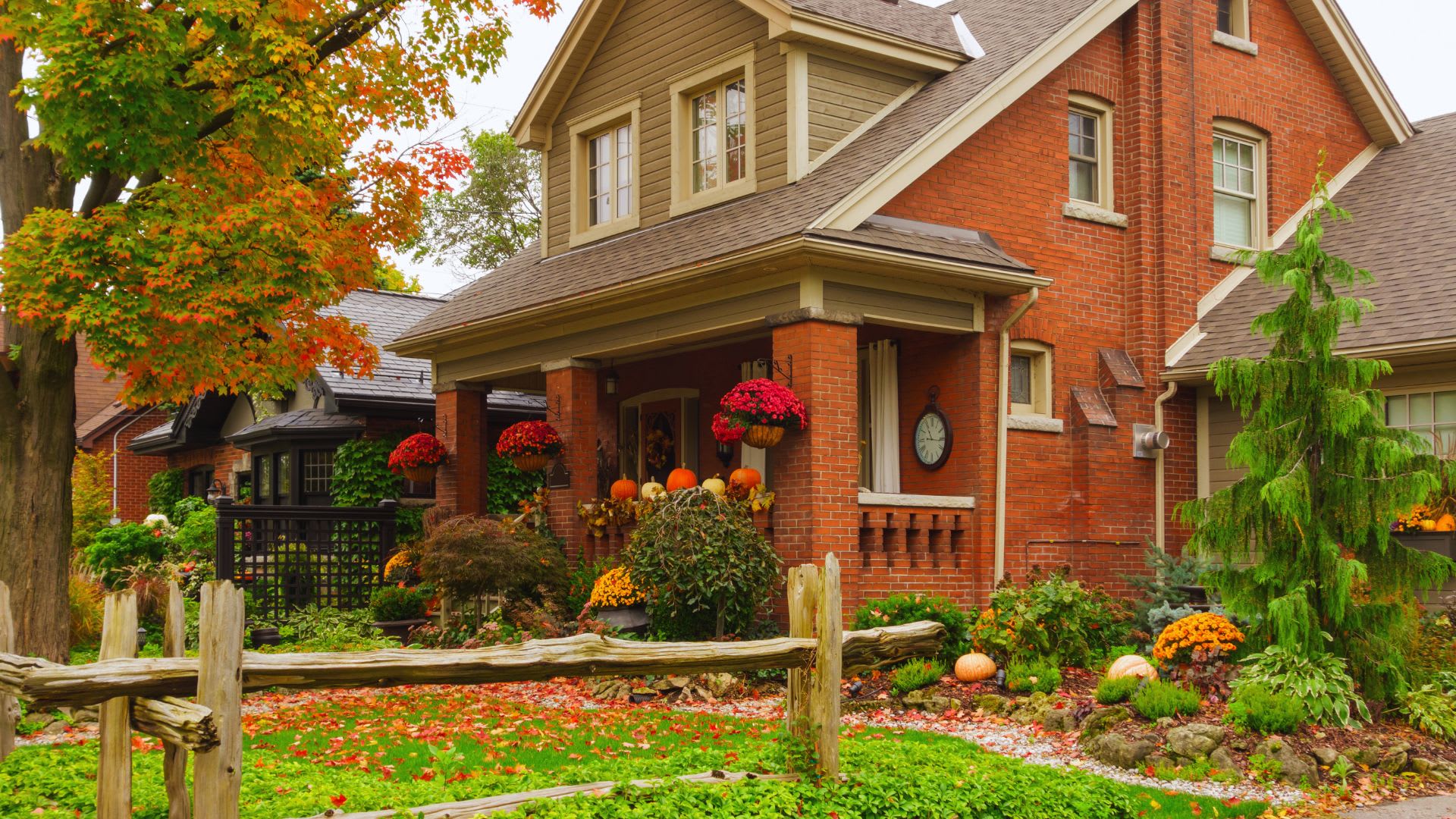 Red brick house with a covered front porch decorated with hanging mums and pumpkins in the fall