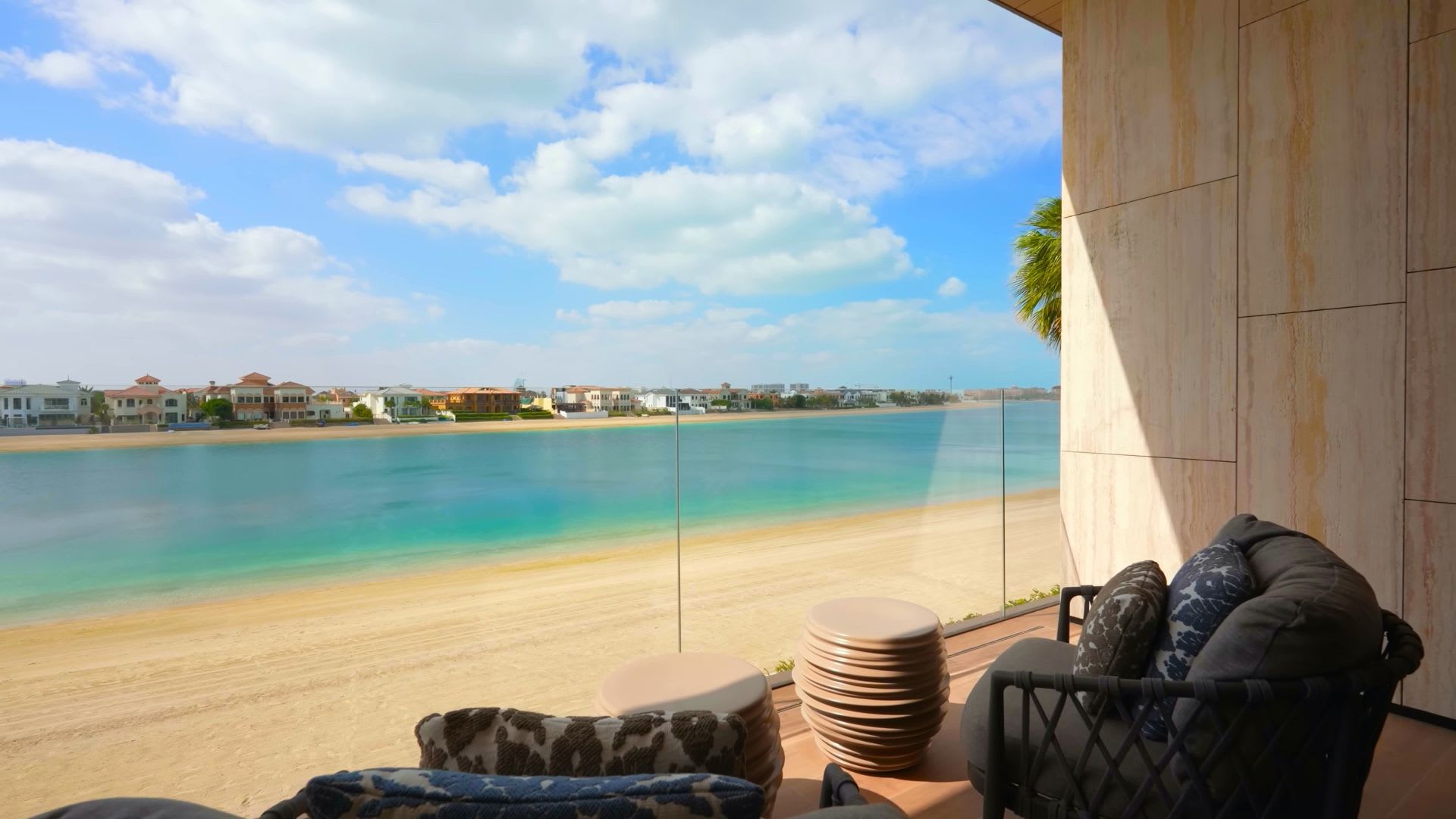 Beachfront balcony with outdoor lounge chairs and a glass railing overlooking a sandy beach and turquoise water