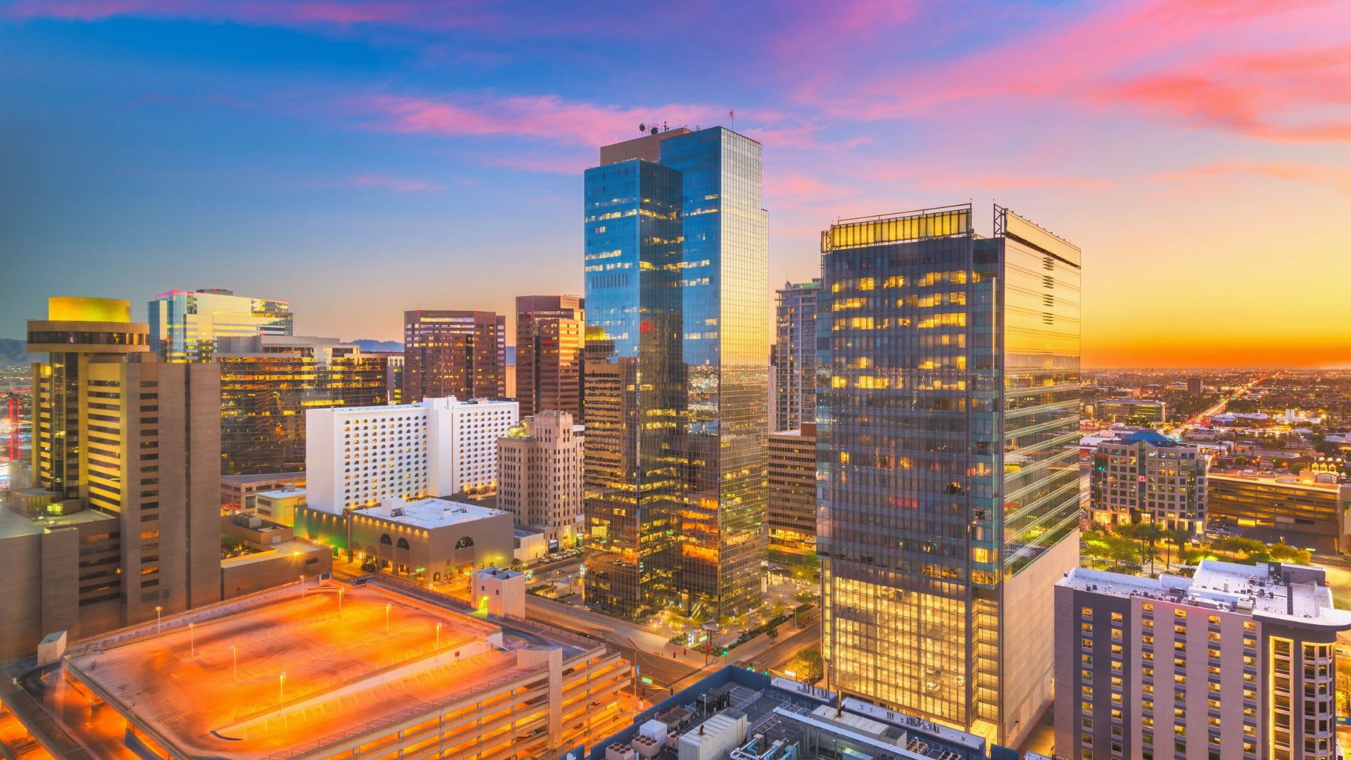 Downtown Phoenix skyline at sunset with glass high-rise towers and city lights stretching to the horizon