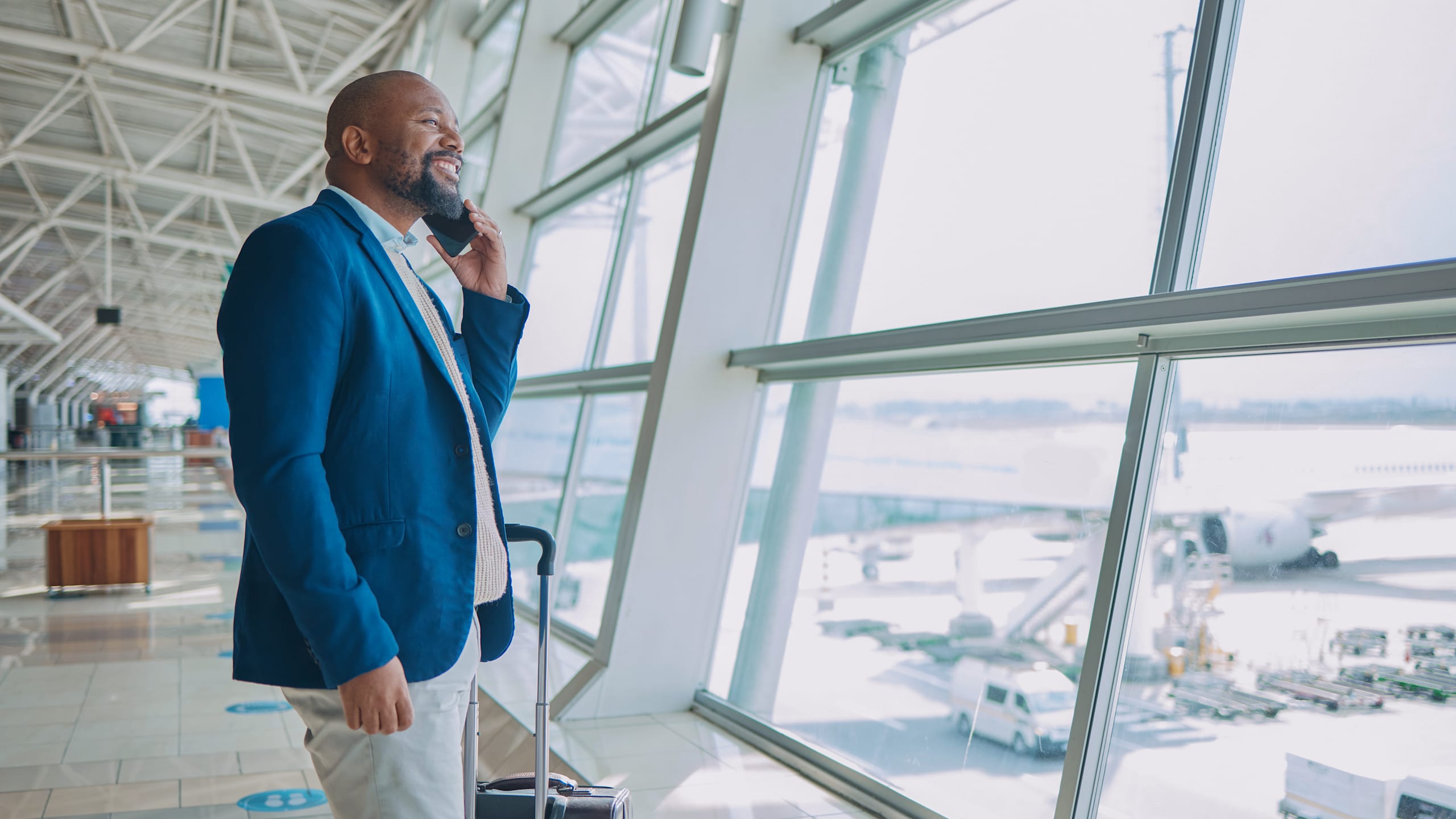 Black man, phone call and luggage at airport for business travel, trip or communication waiting for flight. African American male smile for conversation on smartphone and looking out window for plain man in airport