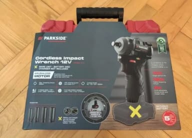 A cordless impact drill in a box on a wooden floor