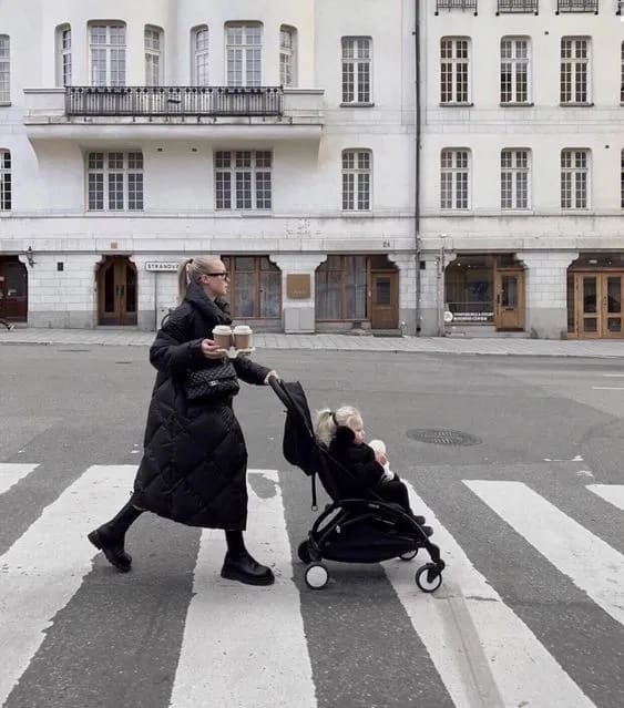 A woman walking across a street with a baby in a stroller
