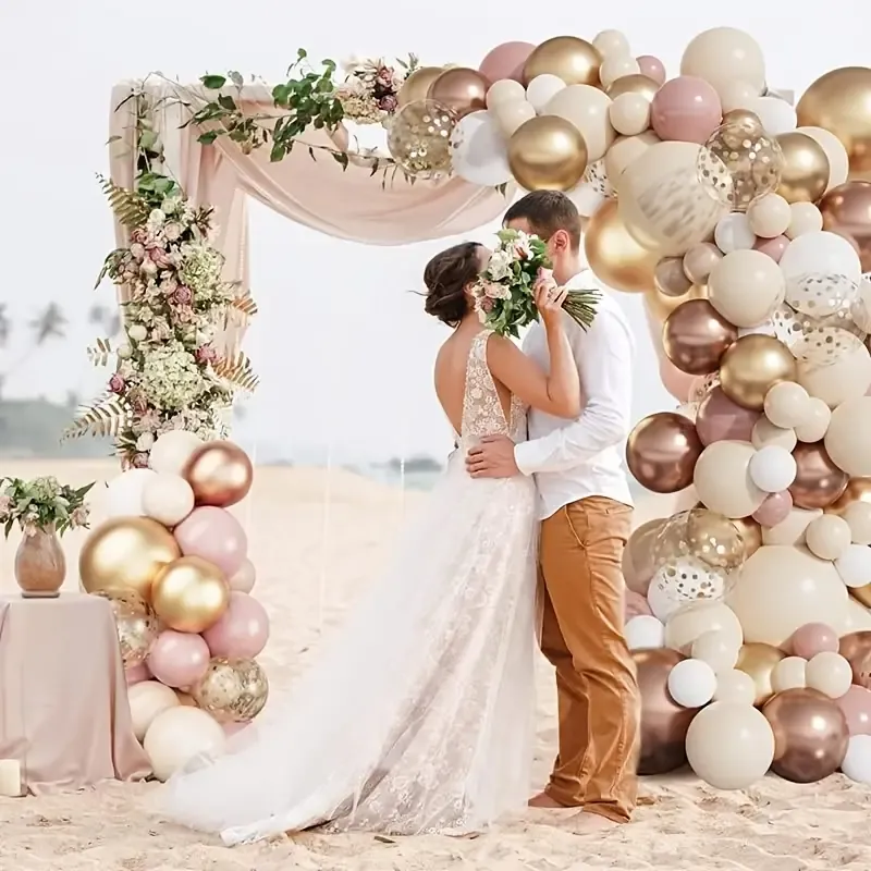 A bride and groom standing under a large arch of balloons