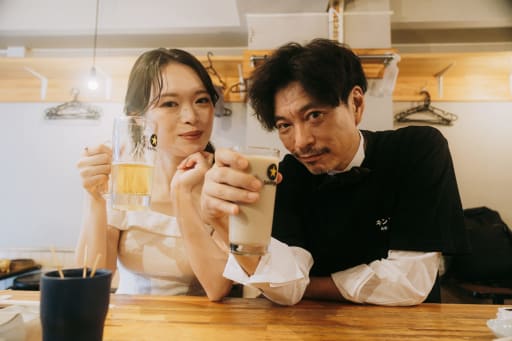 居酒屋のカウンターでグラスを掲げ、カンパイ！
