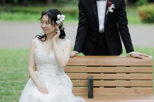 ベンチに腰かける新婦と、後ろで見守る新郎のカット