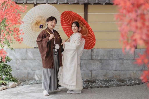 茶の羽織と白無垢で、紅葉を背景にした並び立ち
