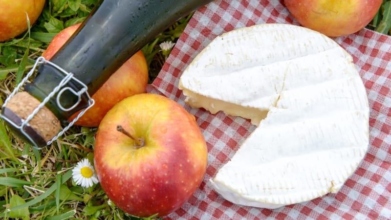 �pplen, en ciderflaska och en mjuk ost ligger p� en rutig piknikfilt