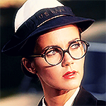 Lynda Carter's Diana wearing a US Navy uniform and hat. Her hair is tied in the back and she wears big round glasses.