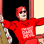 Matt grinning, holding a giant candy cane with his arms extended, and wearing sunglasses, a devil horns diadem, a red Christmas jumper that says 'I'M NOT DAREDEVIL'