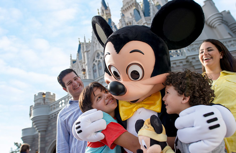 Family hugging Mickey at Disney World near Tropical Escape Vacation Homes.