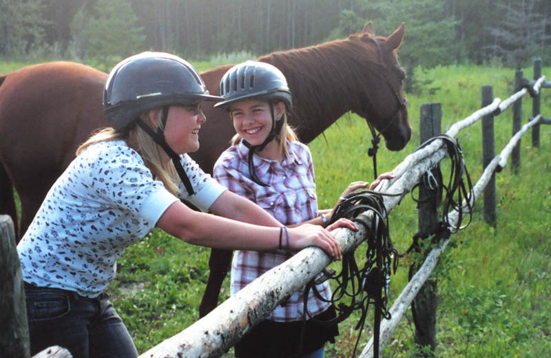 Kids on fence with horses at Trailhead Ranch.