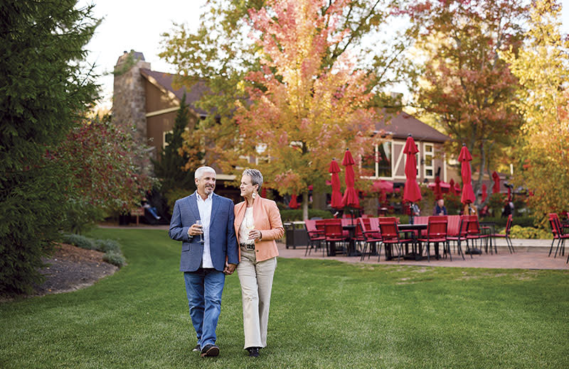 A middle-aged couple smile while walking amid the vineyard property.