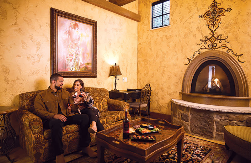 A young newlywed couple embrace each other with smiles while sitting near a fireplace.