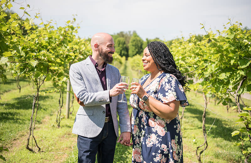 A young couple give cheers while walking amid a vineyard.