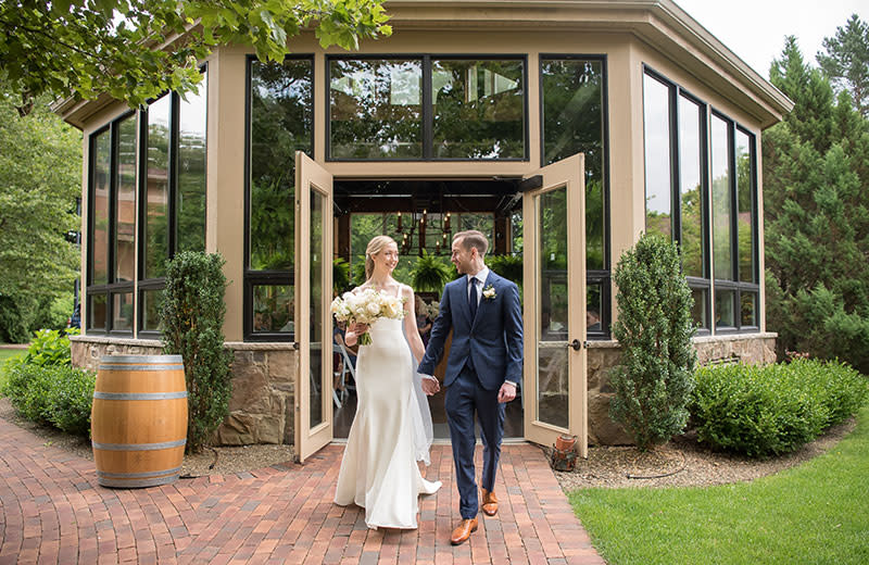 A smiling young newlywed couple exits a conservatory.