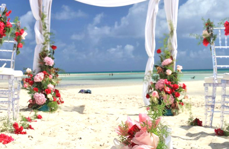 An elegant beach wedding altar adorned with beautiful flowers amid white sand.