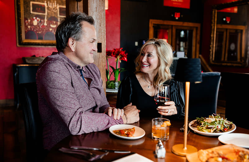 A middle-age newlywed couple smiles at each other while enjoying lunch.