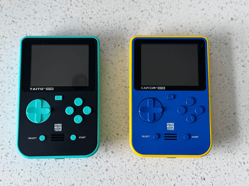 Super Pocket 2 The front of Taito and Capcom Super Pockets out of the packaging on a wooden table top.