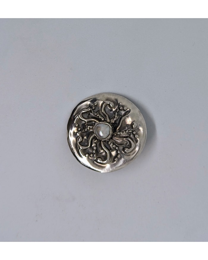 a silver circular object with a pearl