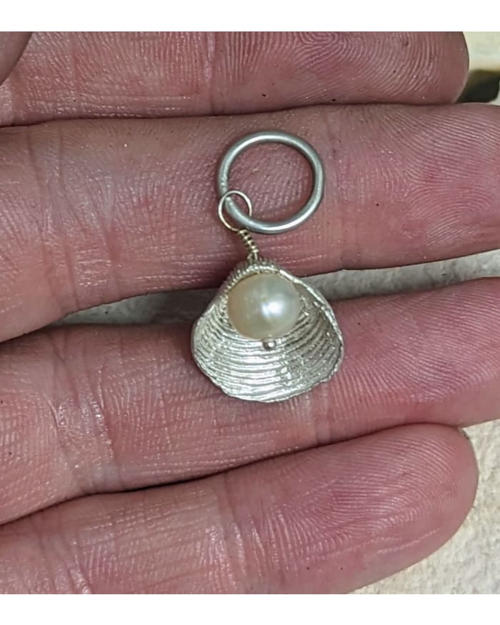 a hand holding a silver shell with a pearl