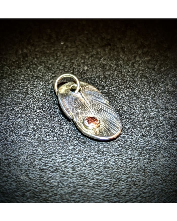 a silver feather with a red gem on a black surface