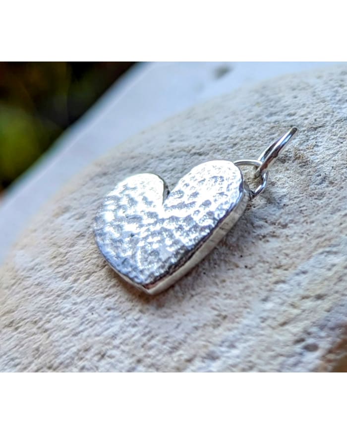 a silver heart shaped pendant on a rock