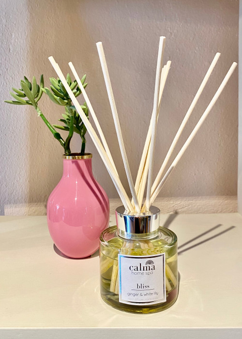 a glass bottle with sticks in it next to a pink vase