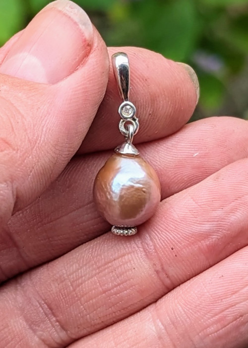 a hand holding a pearl pendant