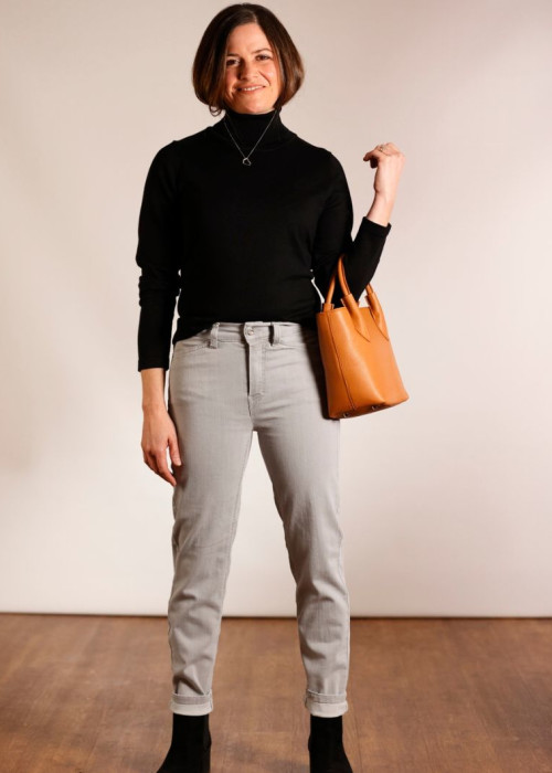 a woman in black turtleneck and grey pants holding a brown purse