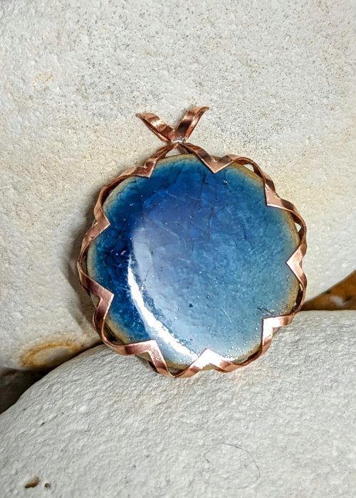a blue and gold pendant on a white rock