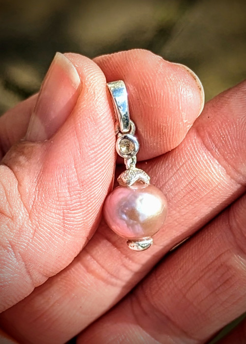 a hand holding a pearl pendant