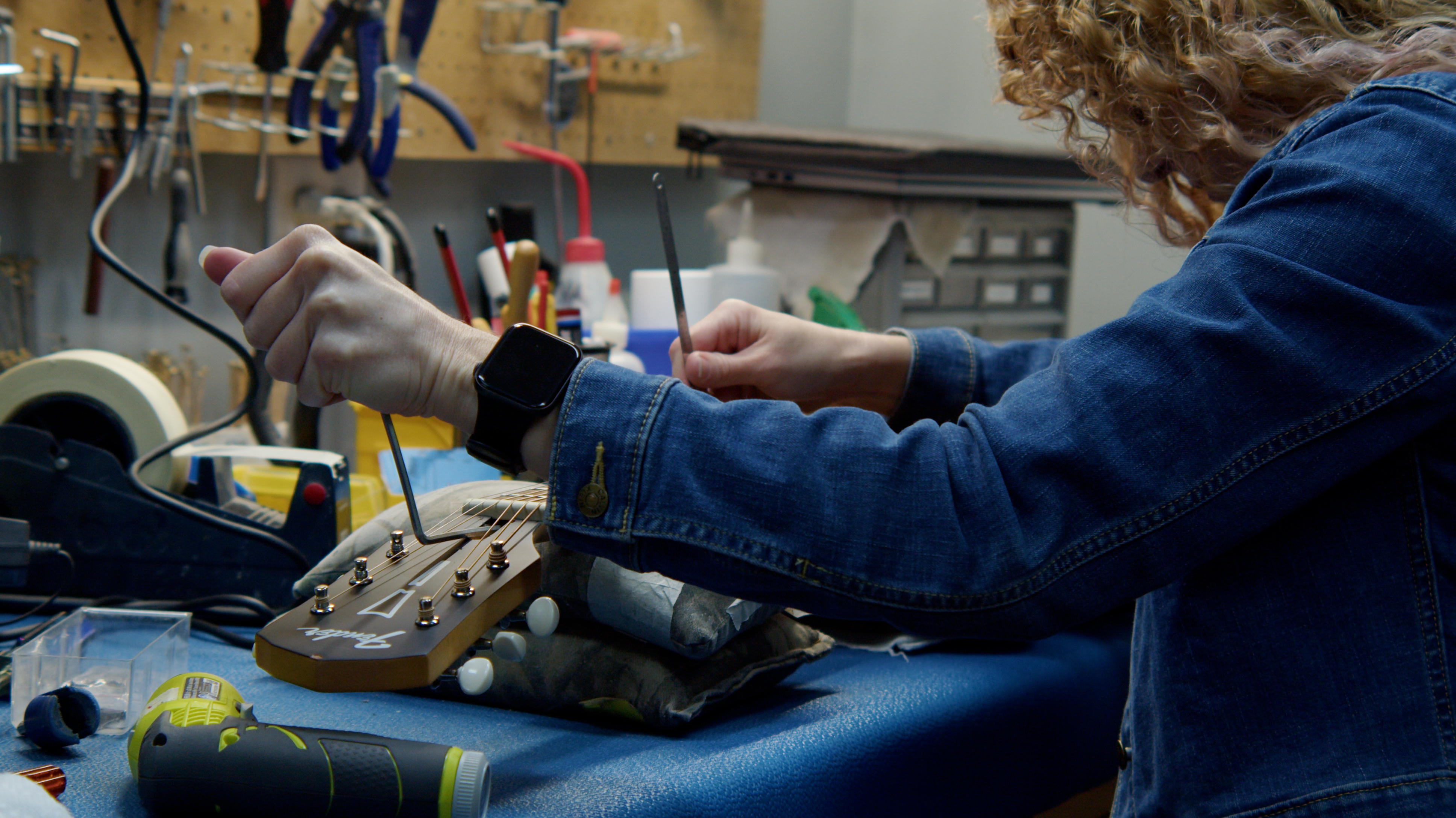 A MIRC staffer adjusts a guitar's truss rod while checking string height.