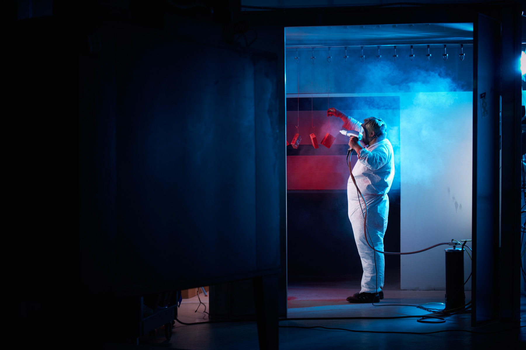 An employee powder coats a collection of enclosures in the spray chamber.