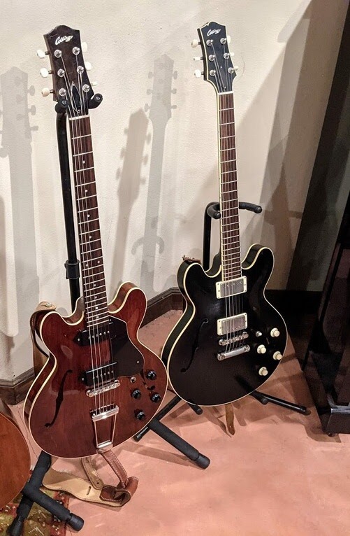 Collings I-30 and I-35 guitars side by side on stands, one red and one black