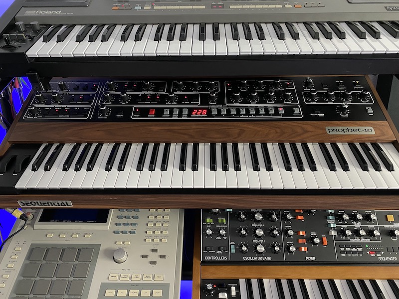 stack of synths: roland, sequential prophet 10, a pad controller, and moog sequencer