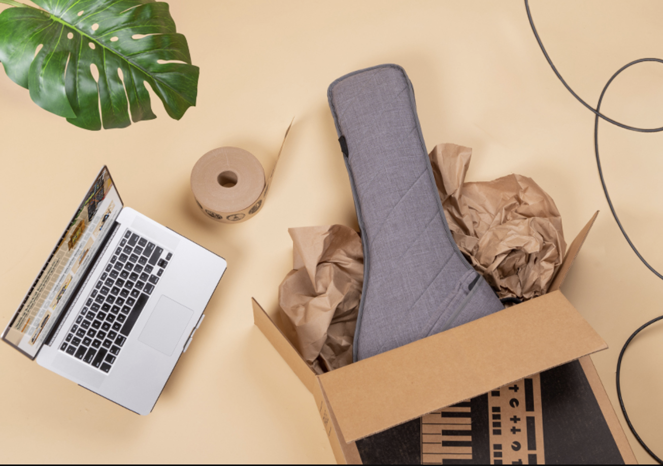 guitar sticking out of box next to laptop and tape and plant leaf