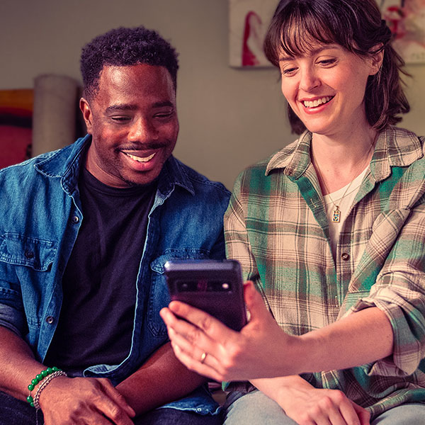 A husband and wife are smiling as they look down at a mobile phone