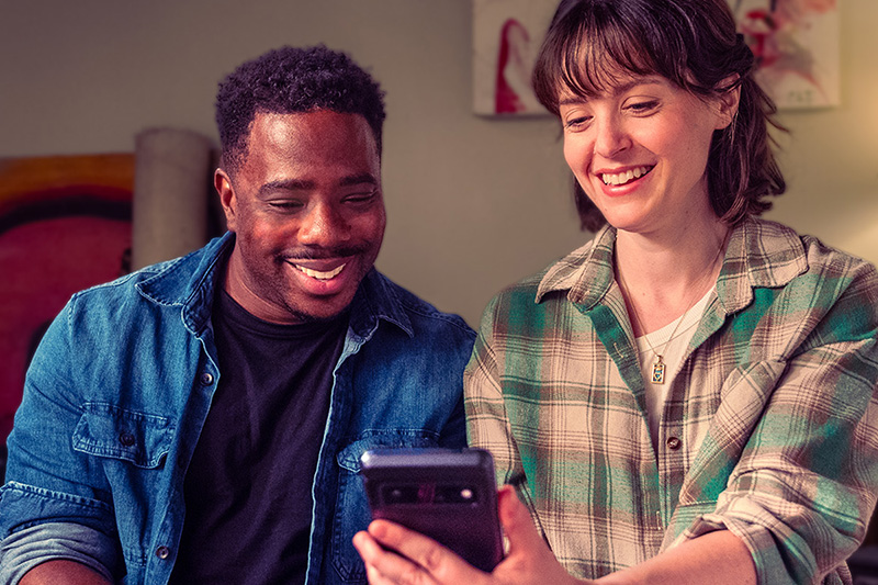 A husband and wife are smiling as they look down at a mobile phone