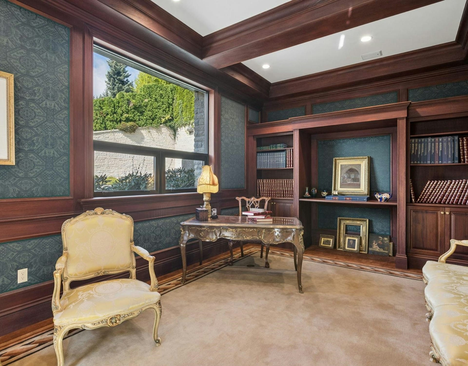 An ornate gold chair and desk sit in the foreground of a study featuring dark wood paneling and built-in bookshelves against the background.