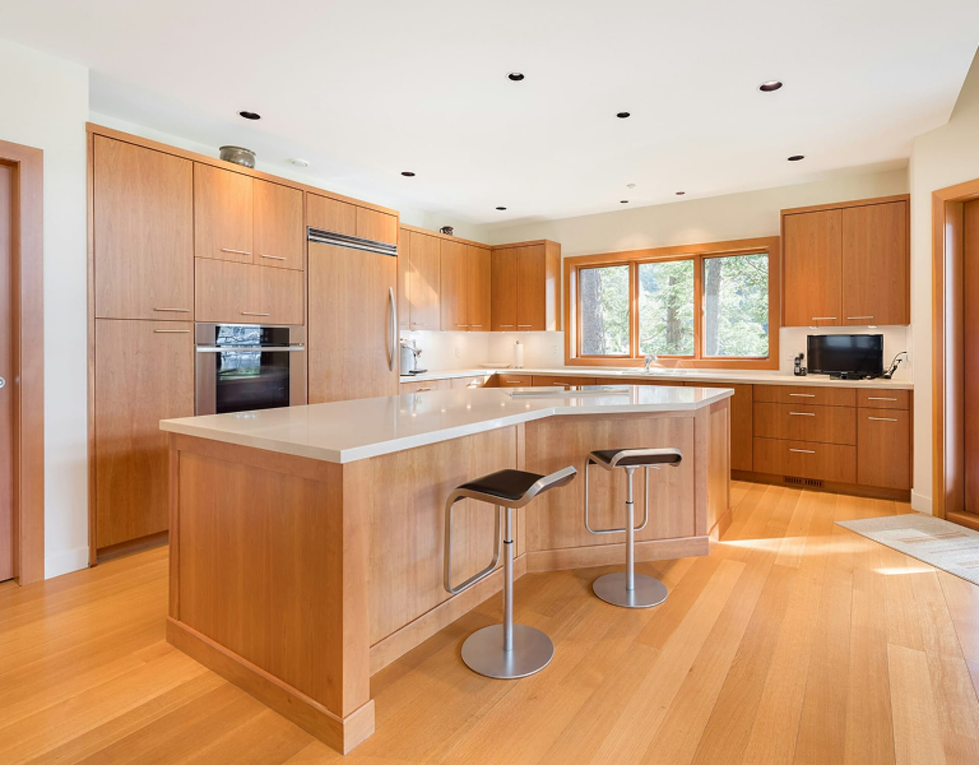 A modern, open-concept kitchen with wooden cabinetry, a central island, and hardwood flooring.