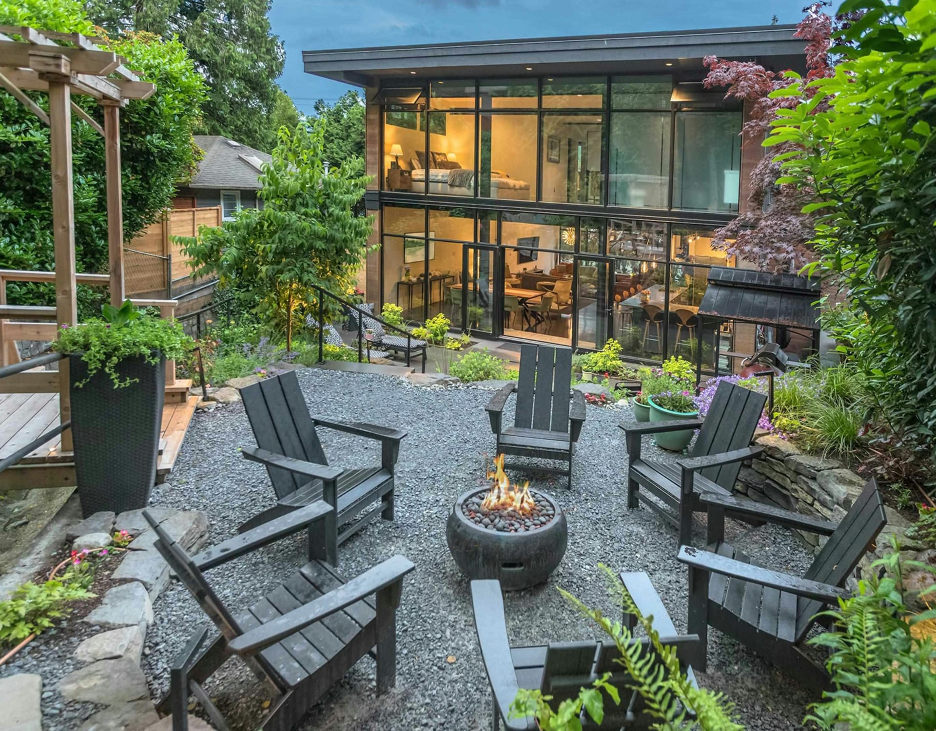 A modern glass-walled house with a lush green backyard.