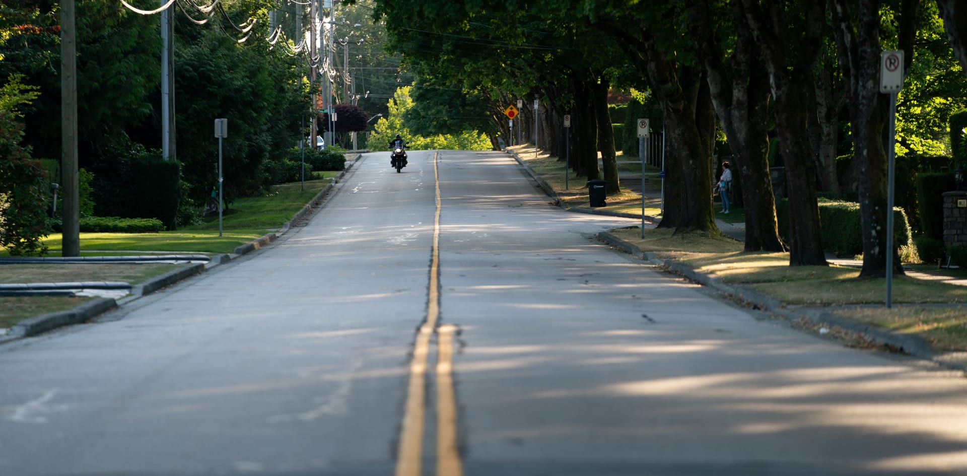 Burnaby residential street with a motorcyclist driving down it.