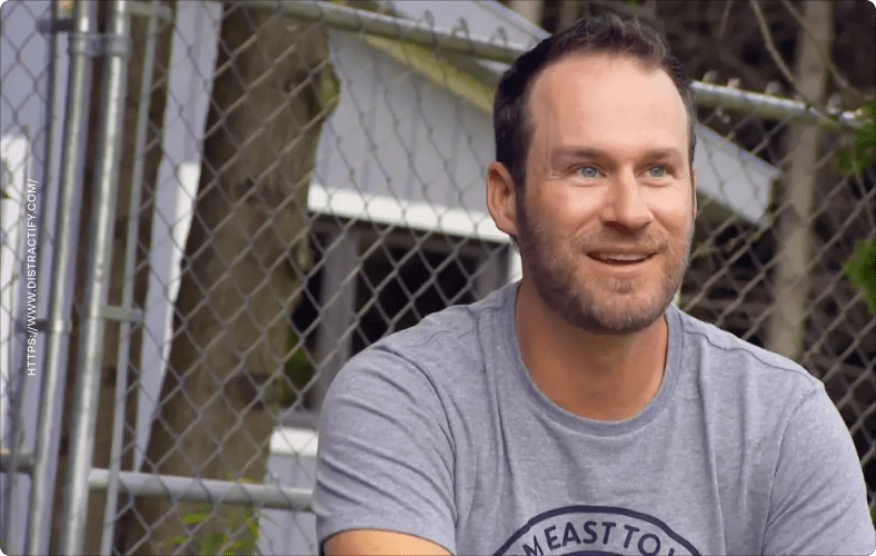 Adam Weir sits outside in front of a chain link fence.
