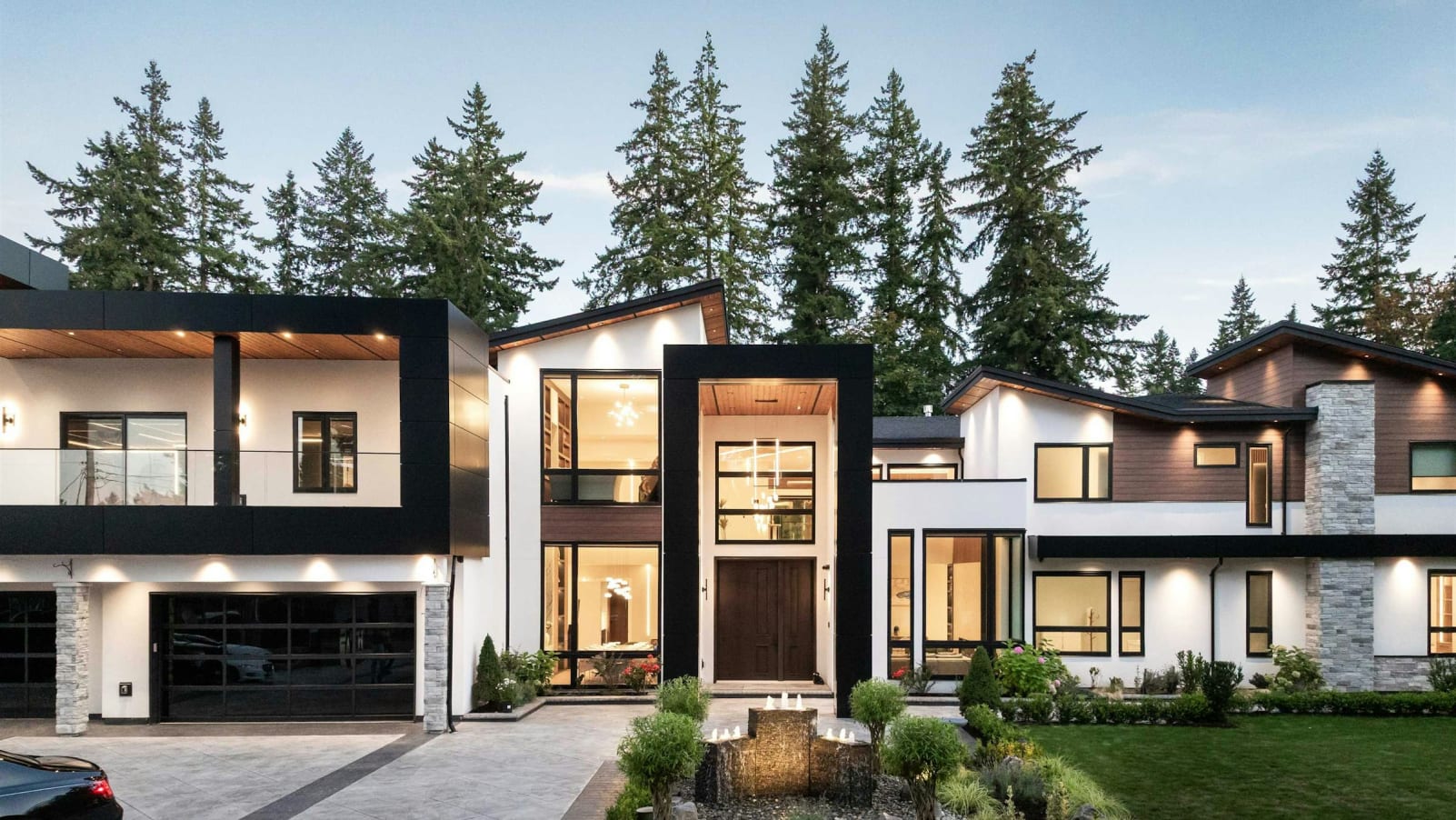 A modern, multi-story residential complex nestled among towering evergreen trees, with a well-manicured lawn and landscaping in the foreground.
