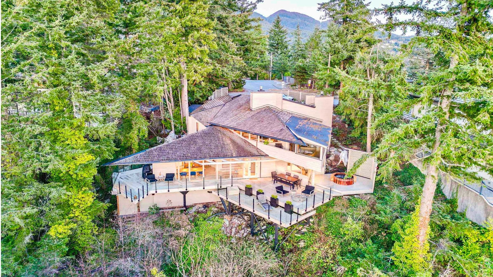A cozy wooden cabin nestled in a lush, verdant forest, with a deck overlooking the surrounding greenery and mountains in the distance.